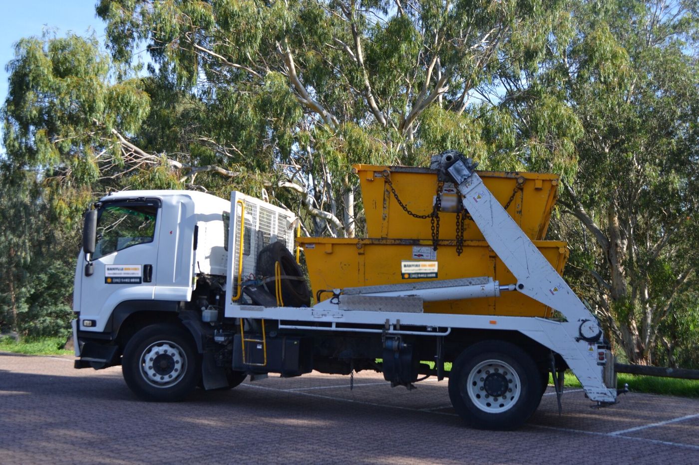 Banyule Bin Hire truck carrying two skip bins past gum trees